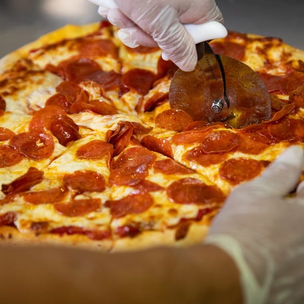 Gloved hands slice a large, hot pepperoni pizza with a pizza cutter at Mama 'n Papa's.